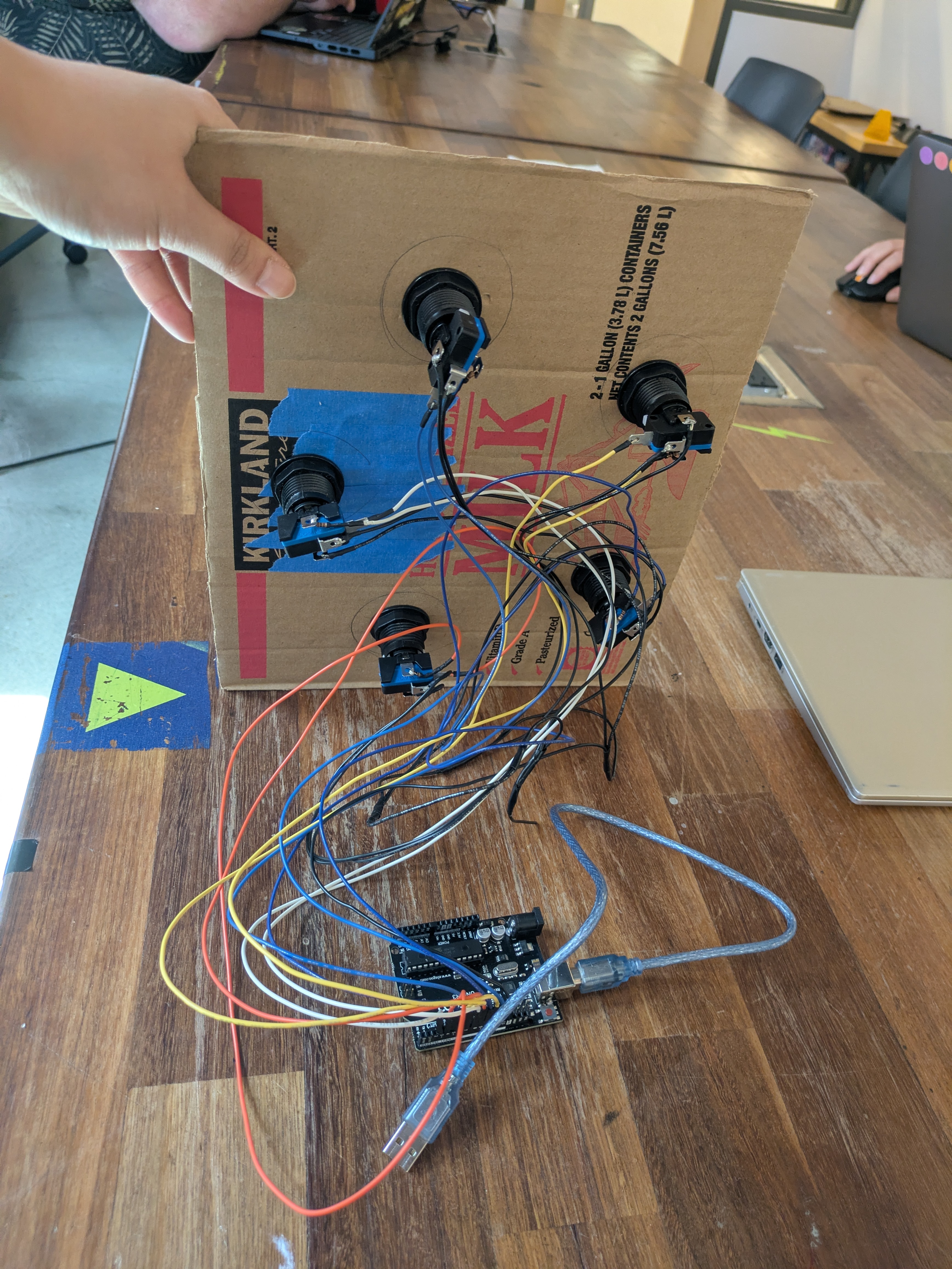 plastic arcade buttons screwed into a piece of cardboard, with a lot of exposed wiring and Arduino board showing