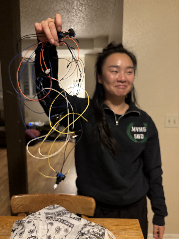 Vikki, an asian woman, holds up a tangle of wires and lights while making a bemused face.